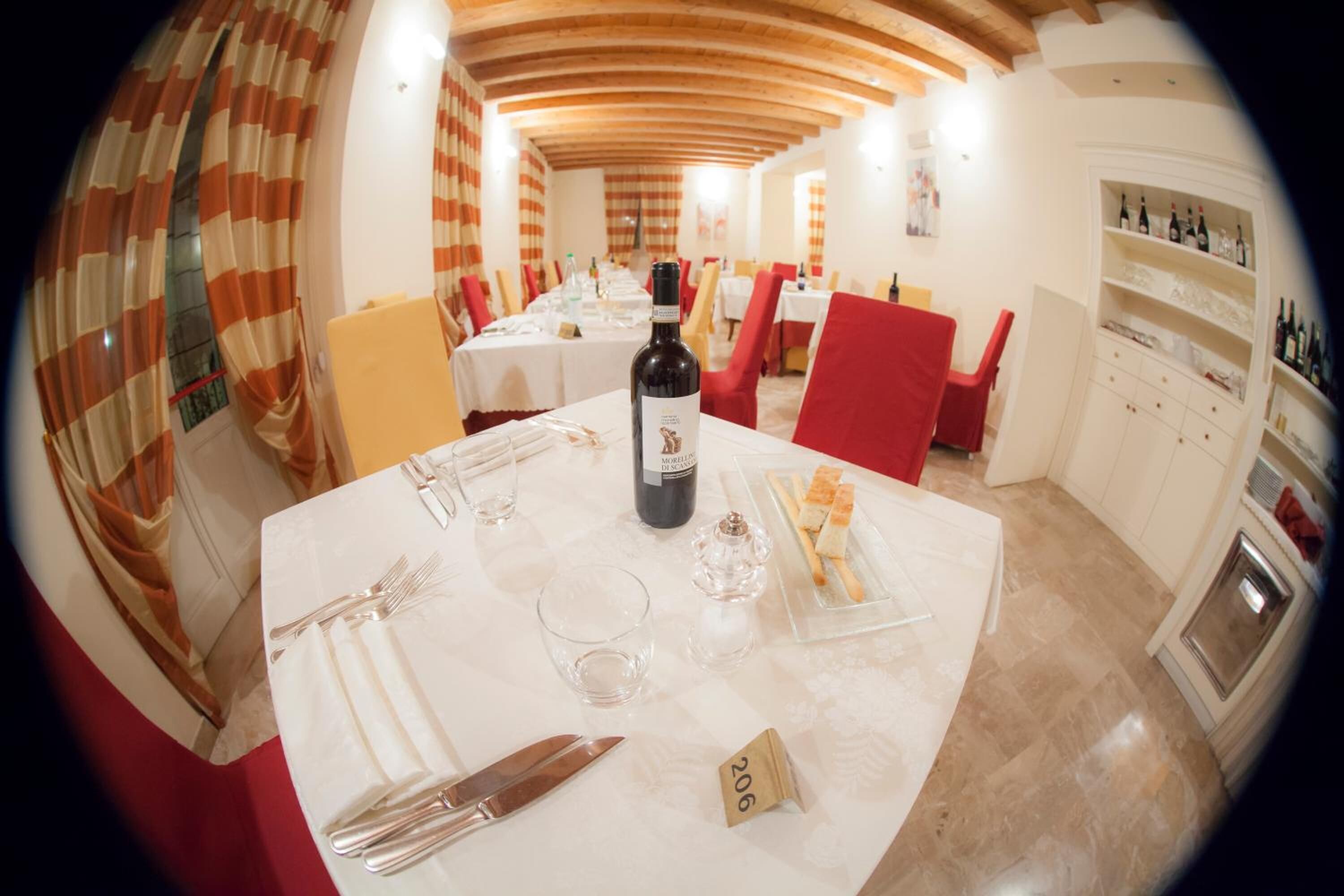 Un'area pranzo con tavoli apparecchiati per due, una bottiglia di vino e un cartello con il numero 206 sul tavolo.