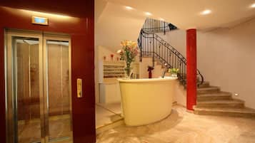 Welcome to our hotel lobby, featuring a reception desk, staircase, and elevator.