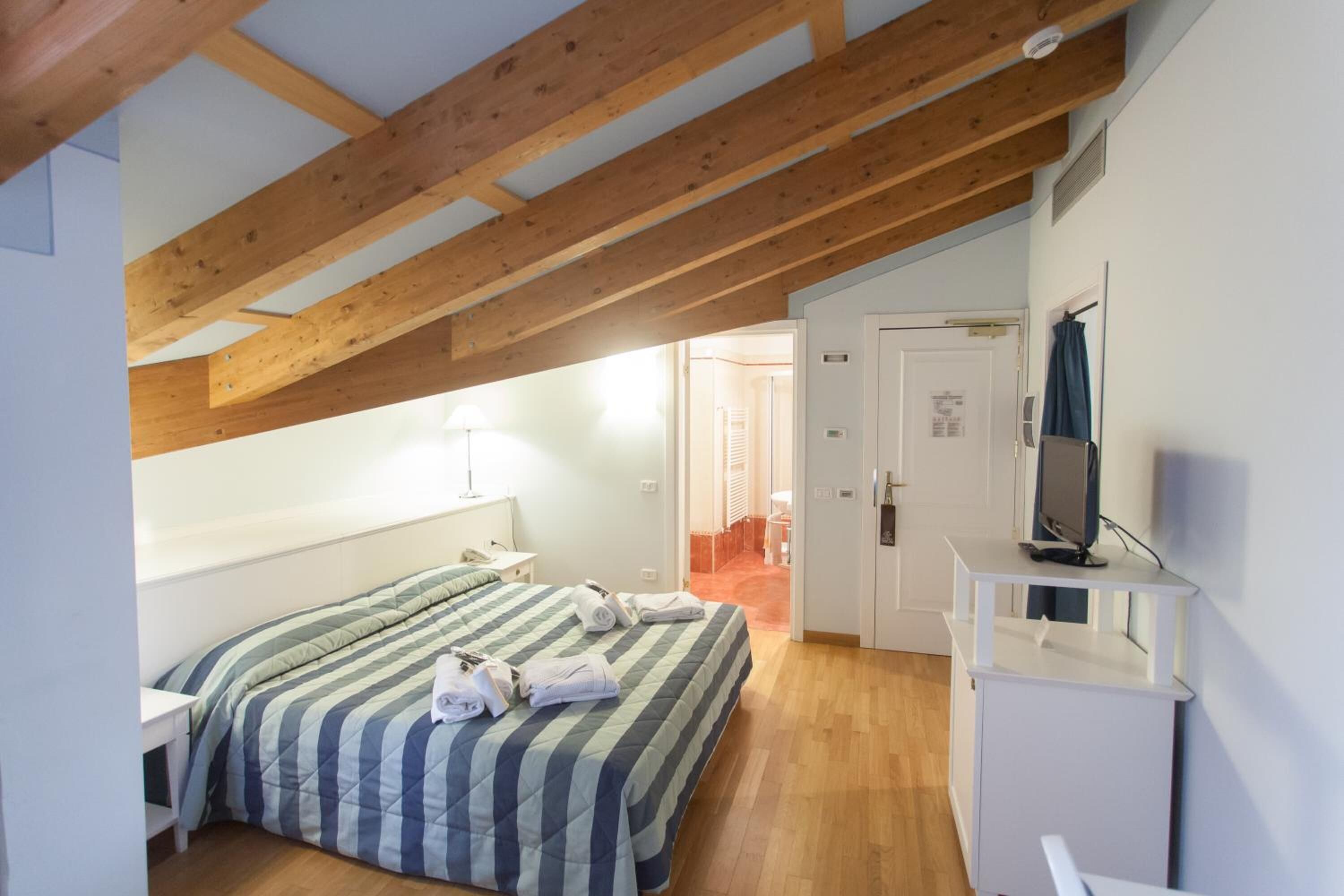 A bedroom with a wooden ceiling, a bed with striped bedding, a TV on a stand, and a door leading to another room.