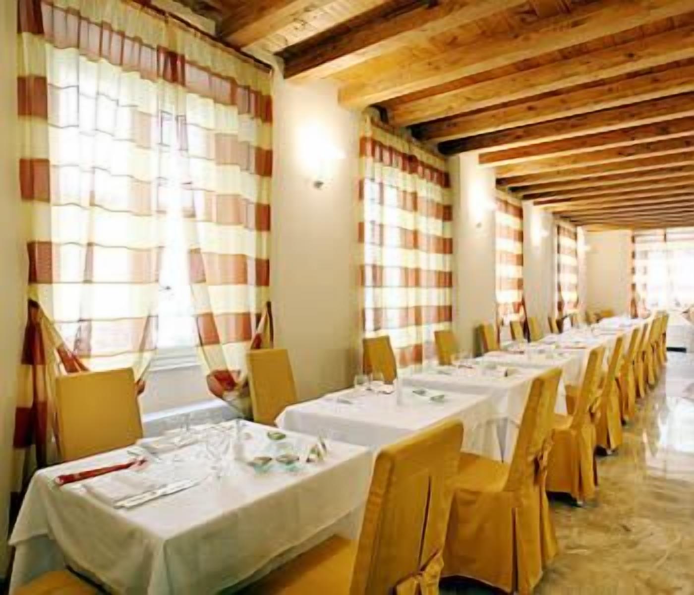 A long dining table with white tablecloths and yellow chairs, set in a room with wooden beams on the ceiling and striped curtains.