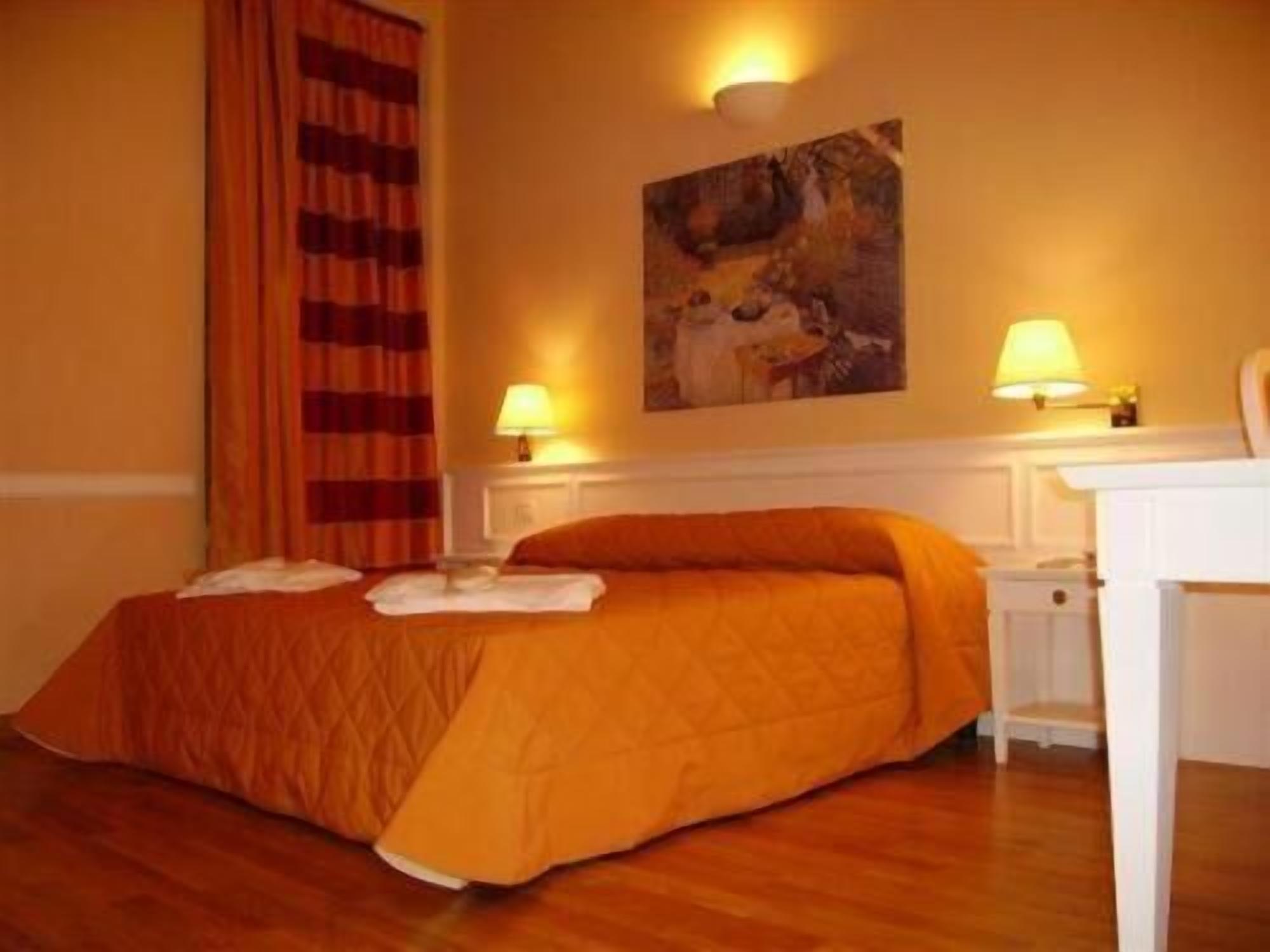Una habitación de hotel con una cama, dos lámparas de noche, un cuadro en la pared y una cortina.