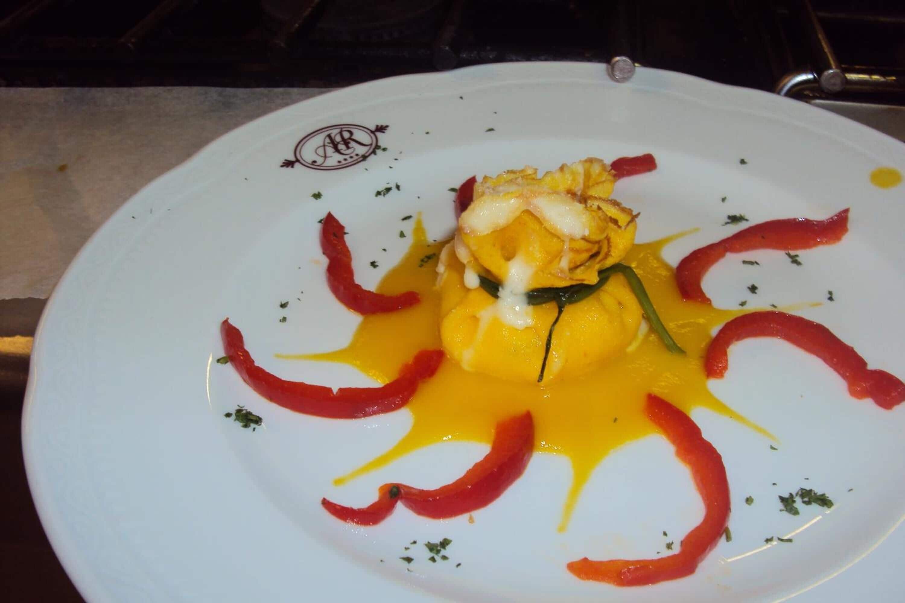 Un plato blanco con un guiso de salsa amarilla, pimientos rojos y hierbas verdes.