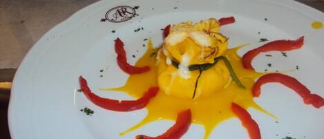 Un plato blanco con un guiso de salsa amarilla, pimientos rojos y hierbas verdes.