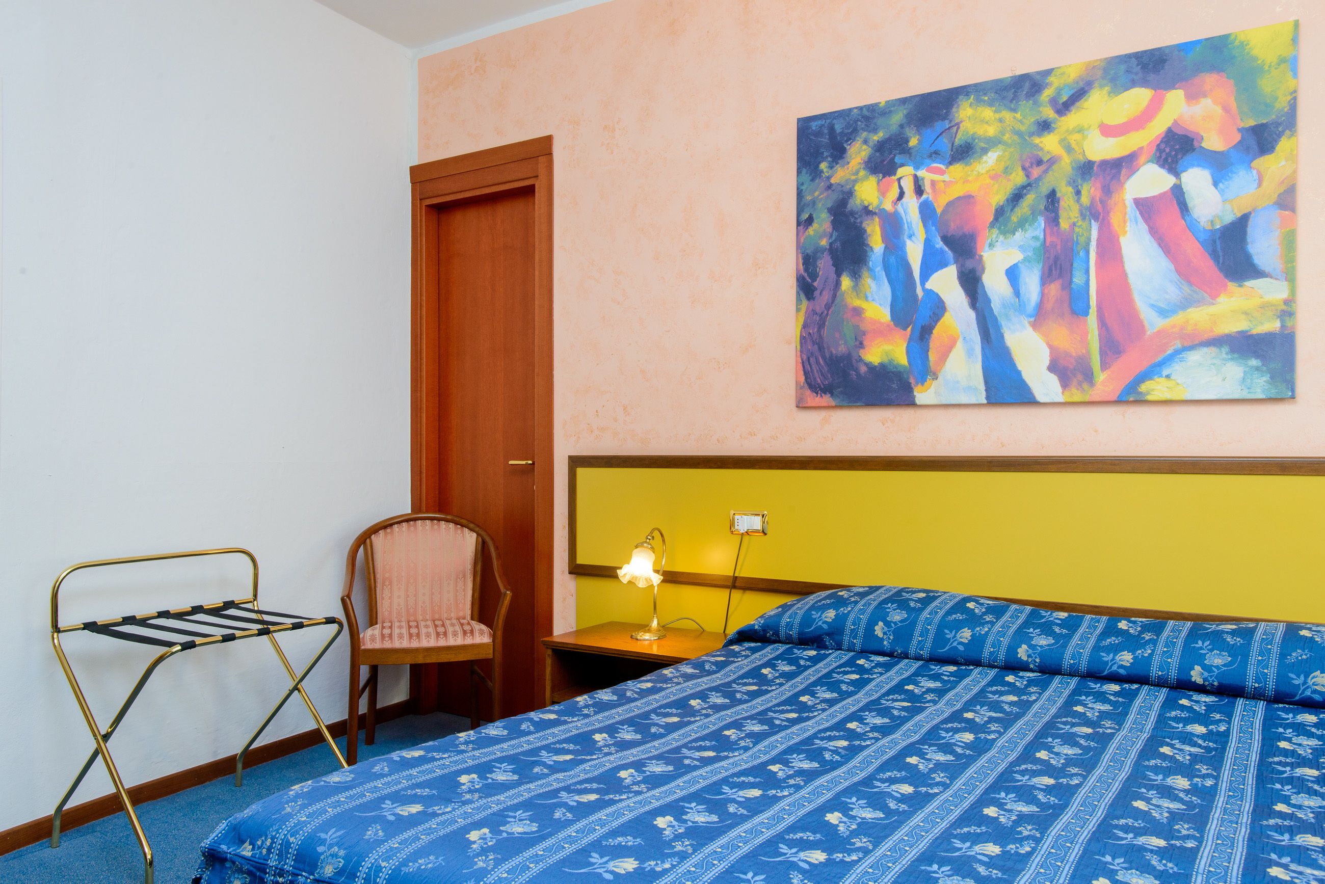Une chambre à coucher avec un lit, une chaise, une table de chevet, une lampe et un tableau au mur.