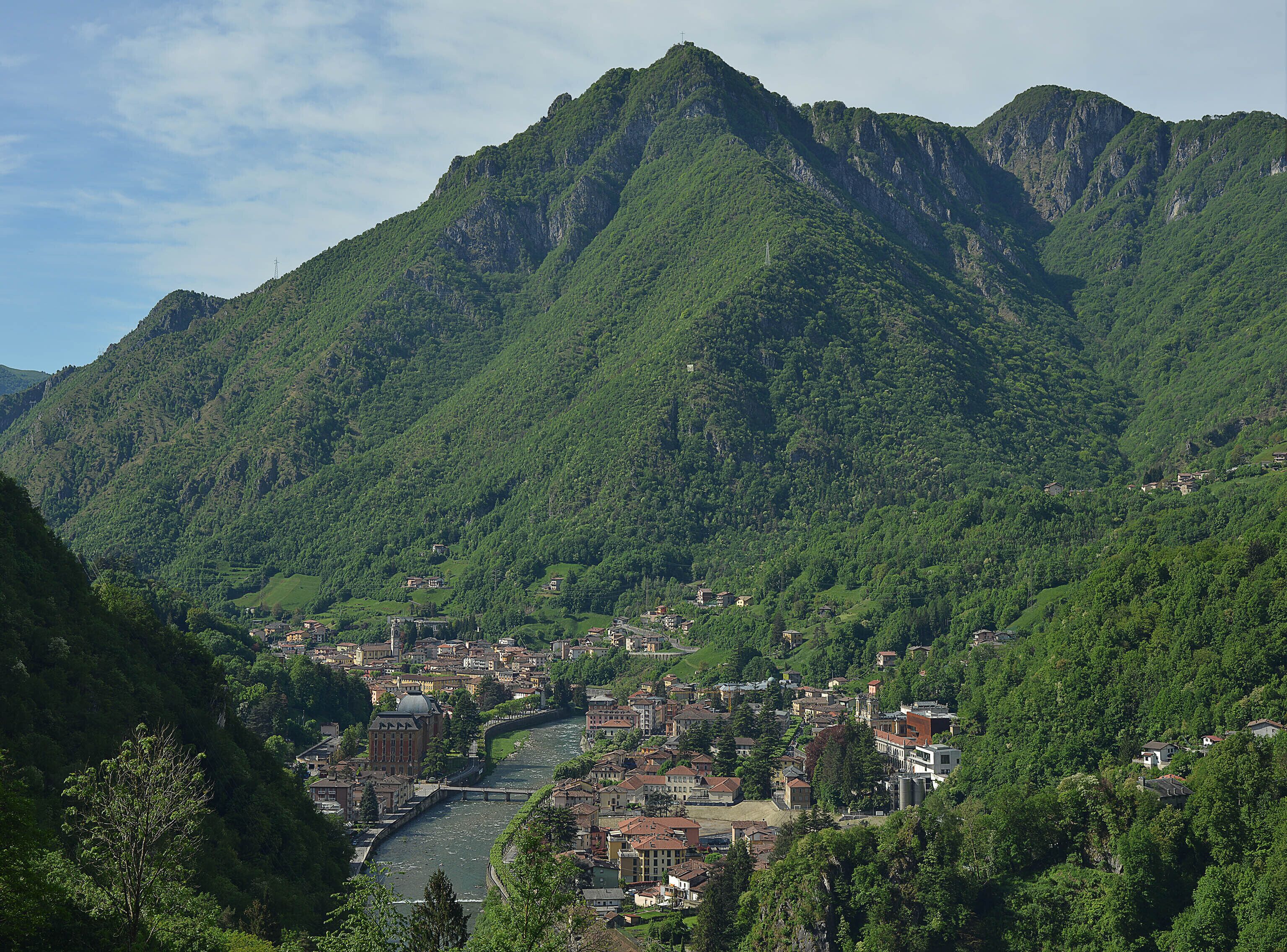 A town nestled in a valley with a river running through it, surrounded by lush green mountains.