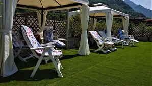 A covered outdoor seating area with lawn chairs and umbrellas, set against a backdrop of mountains. - Bes Hotel Papa San Pellegrino Terme (San Pellegrino Terme)