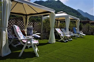 Un espacio de estar al aire libre con techo, con sillas de jardín y sombrillas, con montañas como telón de fondo.