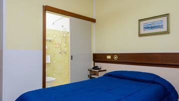 Un dormitorio con cama, una mesita de noche, un cuadro enmarcado en la pared y un baño visible a través de una puerta abierta.