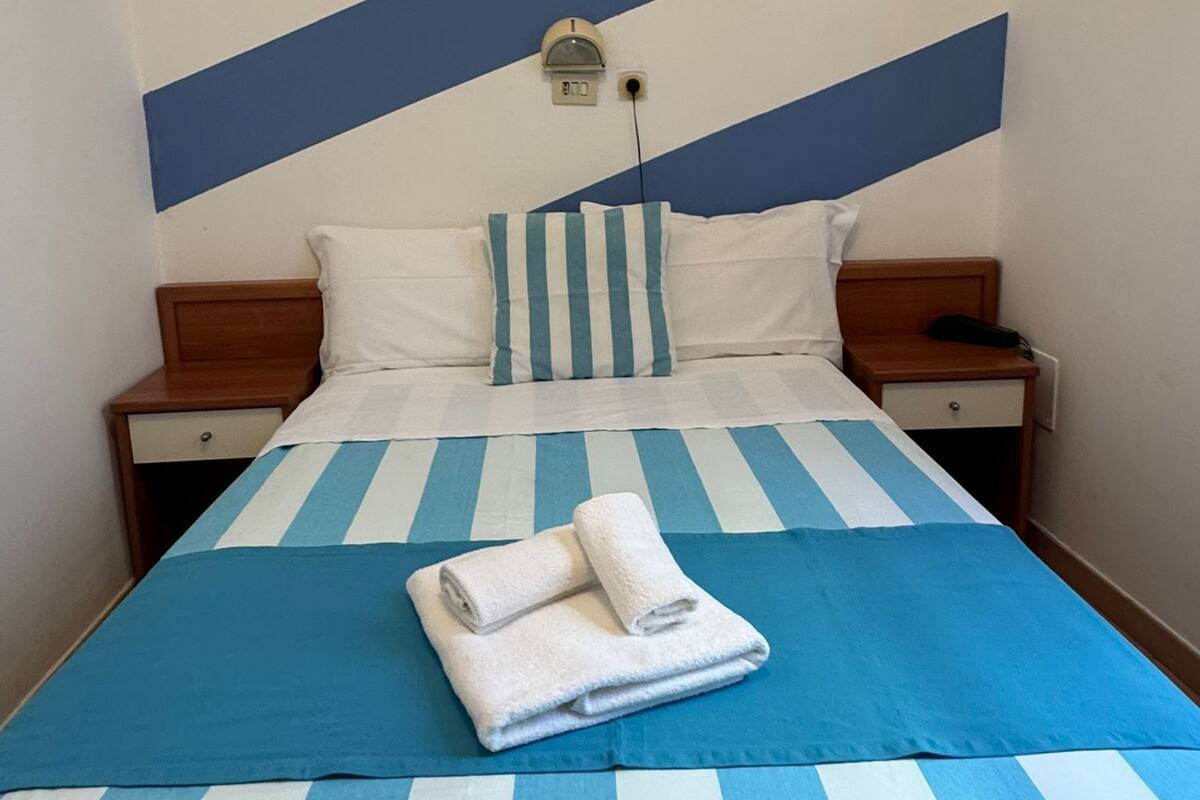 Hotellihuone, jossa on sänky, yöpöytä, sängyn vieressä oleva pöytä ja seinäkello.