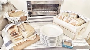 A kitchen area with a bread oven, a stack of white plates, and a wooden cutting board. - Hotel Villa Caterina (Rimini)