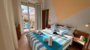 A hotel room with a bed, a nightstand, a lamp, a window with curtains, and a view of the outside. - Hotel Villa Caterina (Rimini)