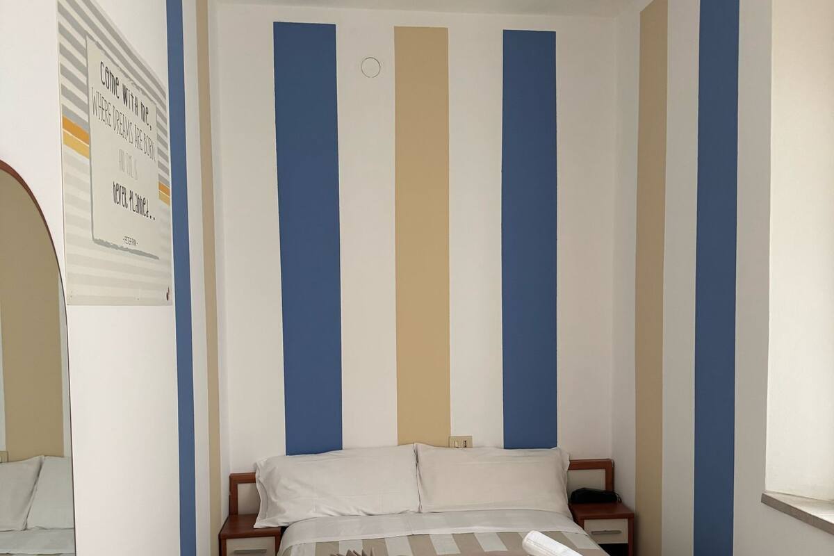 Hotellihuone, jossa on sänky, puinen tuoli, pieni pöytä ja yöpöytä.