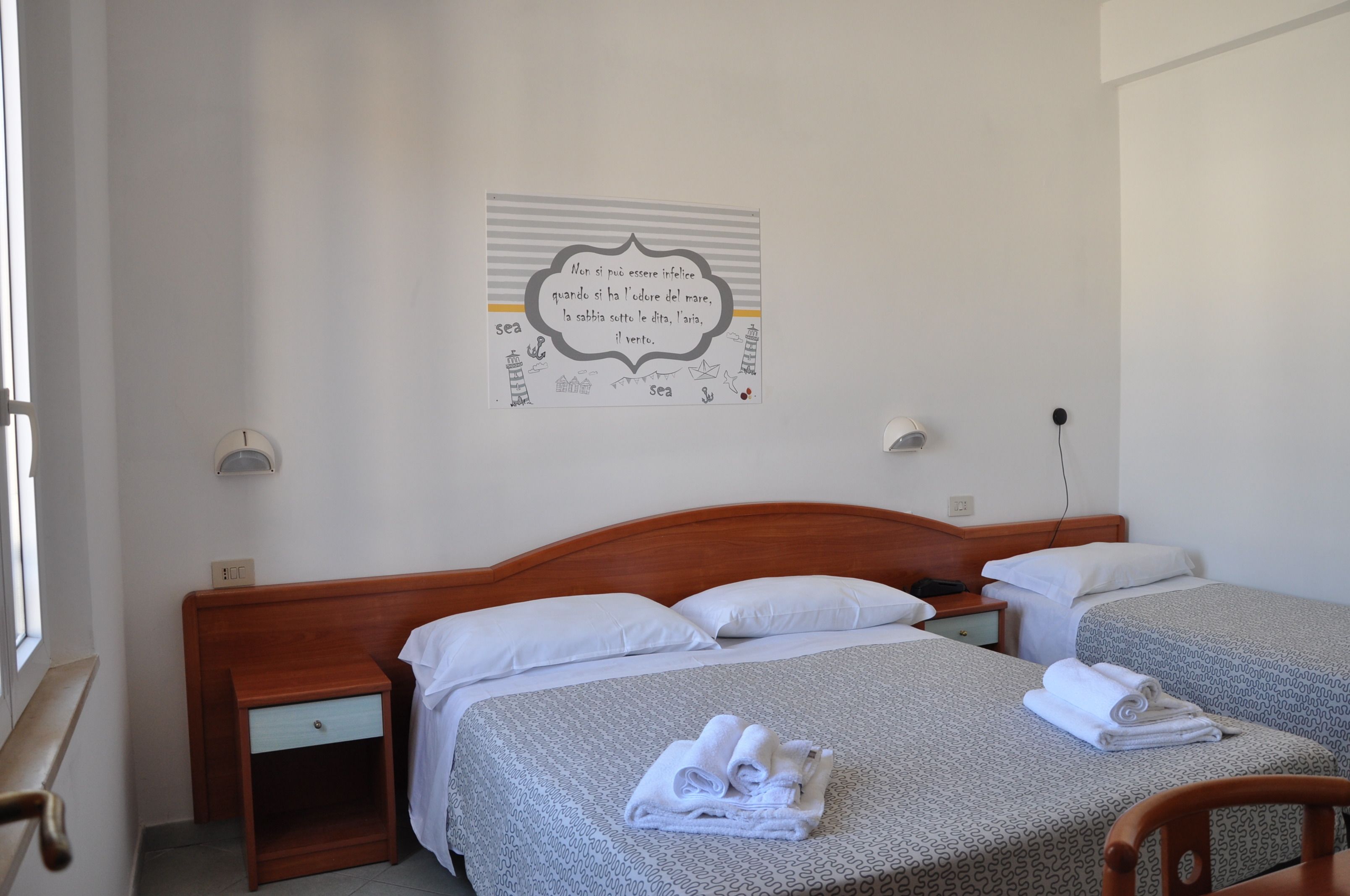 A hotel room with two beds, a wooden headboard, a bedside table, and a wall-mounted artwork.