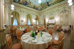 A banquet hall with round tables set for dining, ornate ceiling frescoes, and classical architectural details.