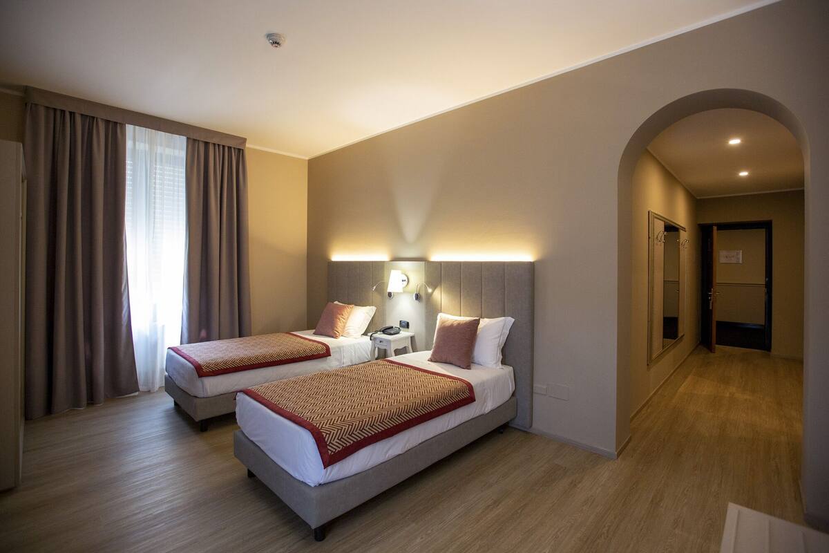 A hotel room with two beds, a nightstand, a lamp, and a mirror.