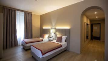 Quarto de hotel com duas camas, uma mesa de cabeceira, uma luminária e um espelho.