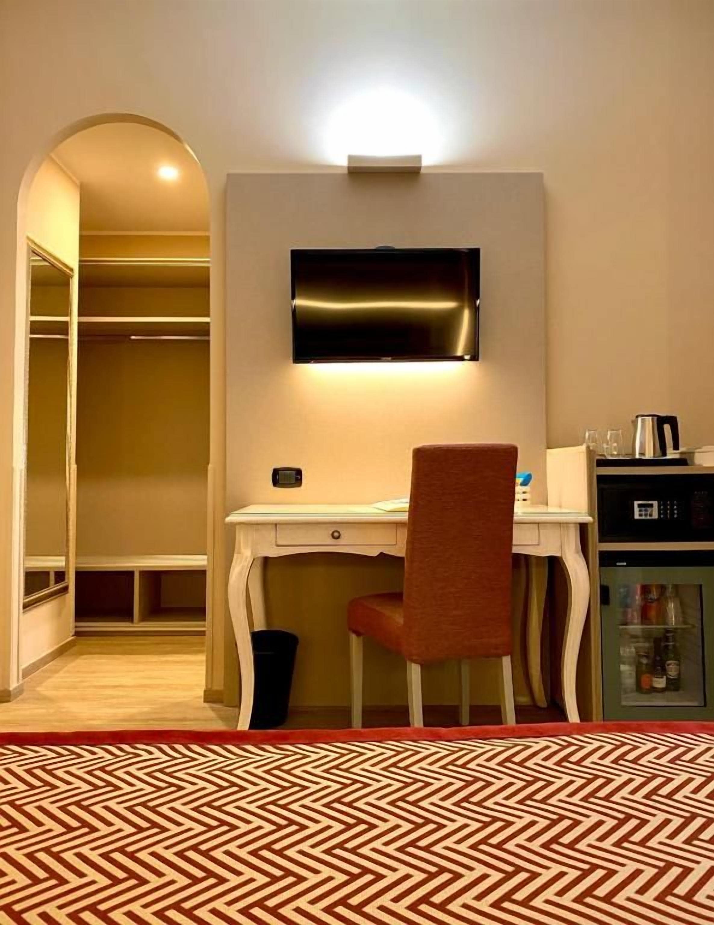 Habitación de hotel con escritorio, silla, televisor y minibar.