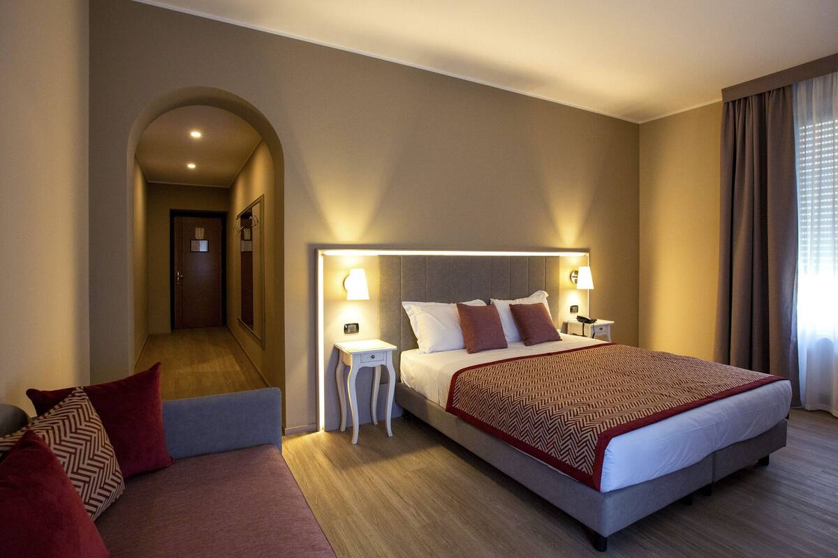 A hotel room with a large bed, bedside tables, a mirror, and a view of the hallway.