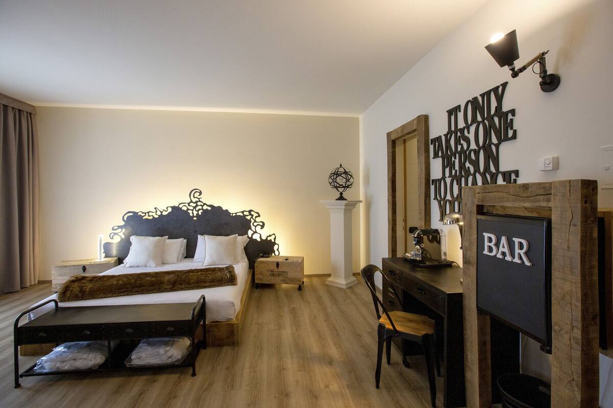 A bedroom with a bed, bedside tables, a desk, and a chair. There is a wall sign that reads "Takes One Person to Change One."