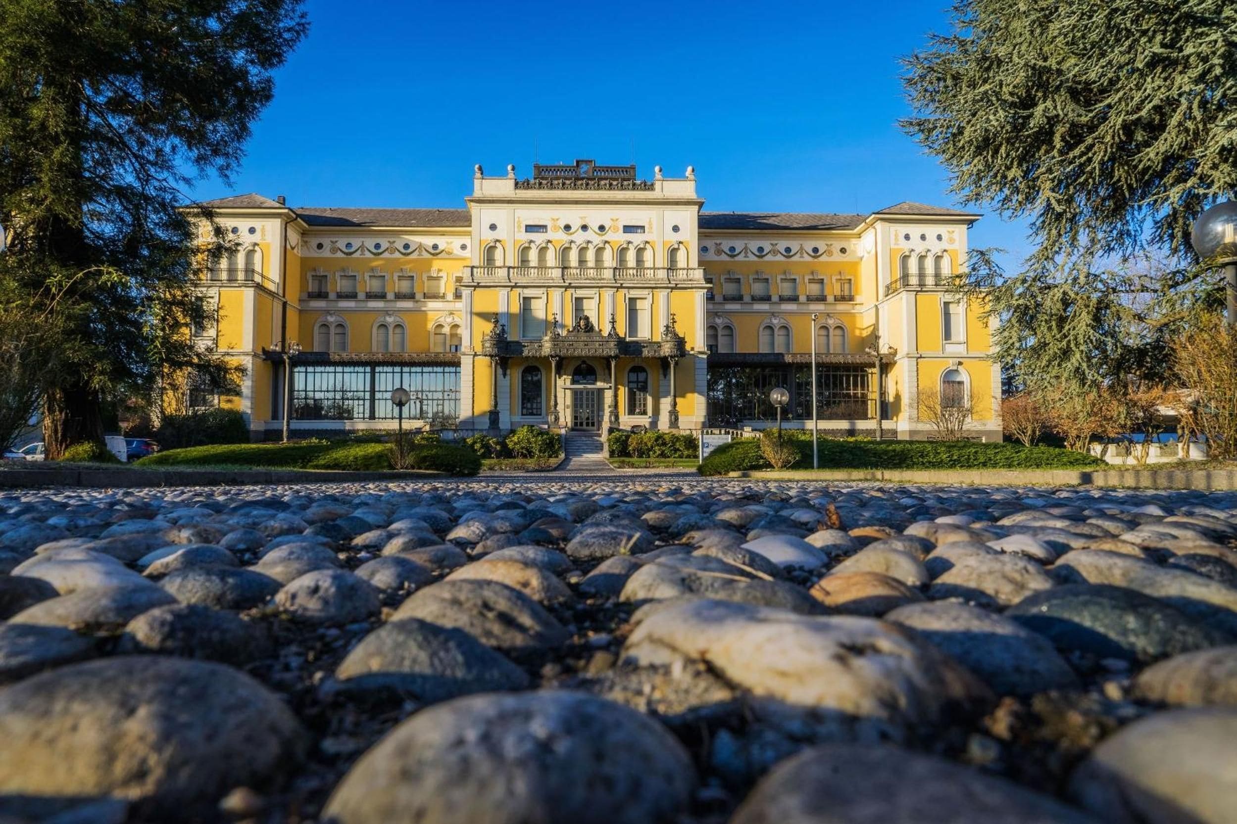 A large, historic building with a symmetrical facade, a central entrance with a portico, and a paved courtyard with large stones.