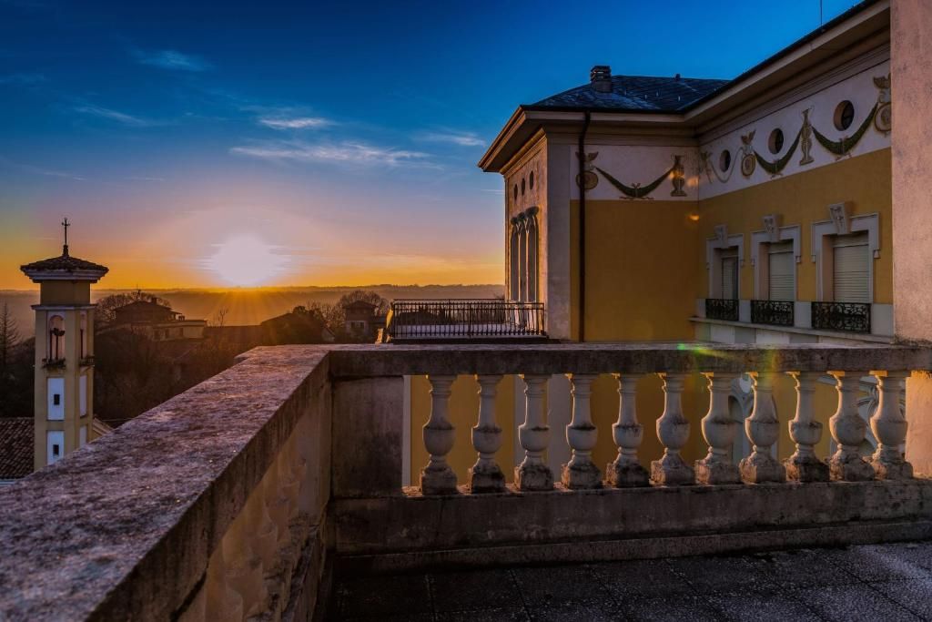 Un edificio con balcón, una torre y un atardecer de fondo.