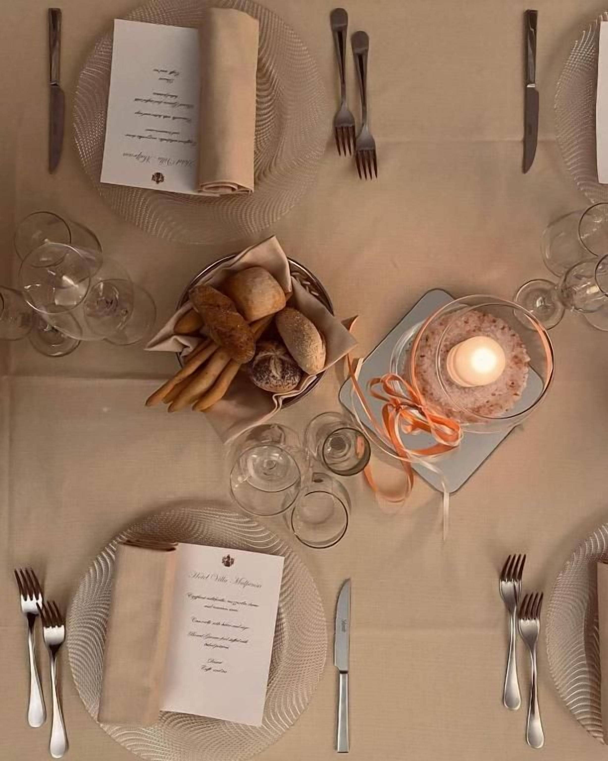 Una mesa dispuesta para una comida, con un menú, vasos, pan y una vela.