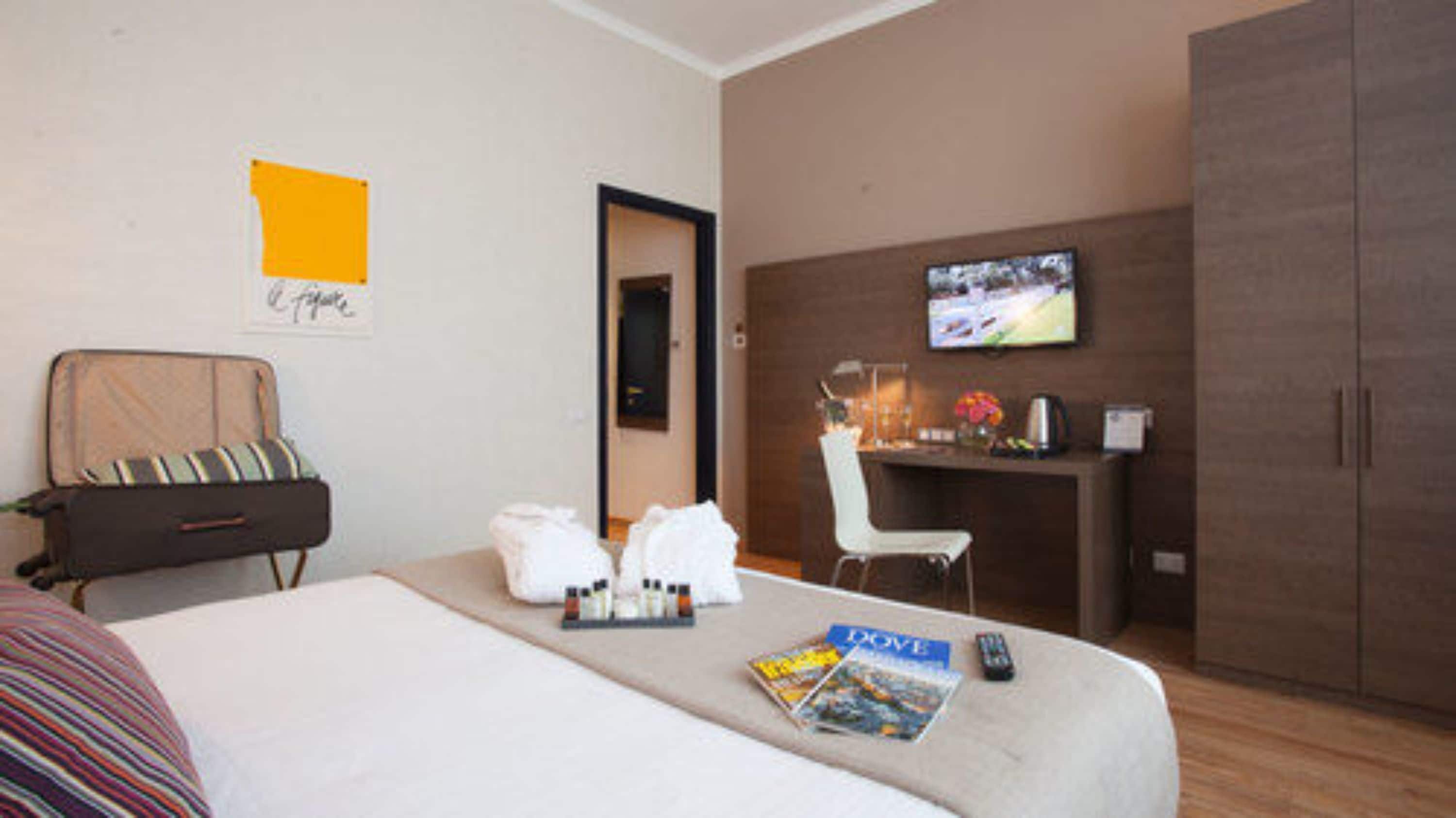 A hotel room with a bed, a desk with a TV, a chair, and a wardrobe.