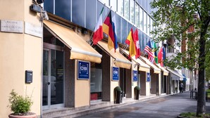 A hotel facade with multiple flags, a clear entrance, and a sign indicating amenities. - Hotel Oro Blu (Milan)