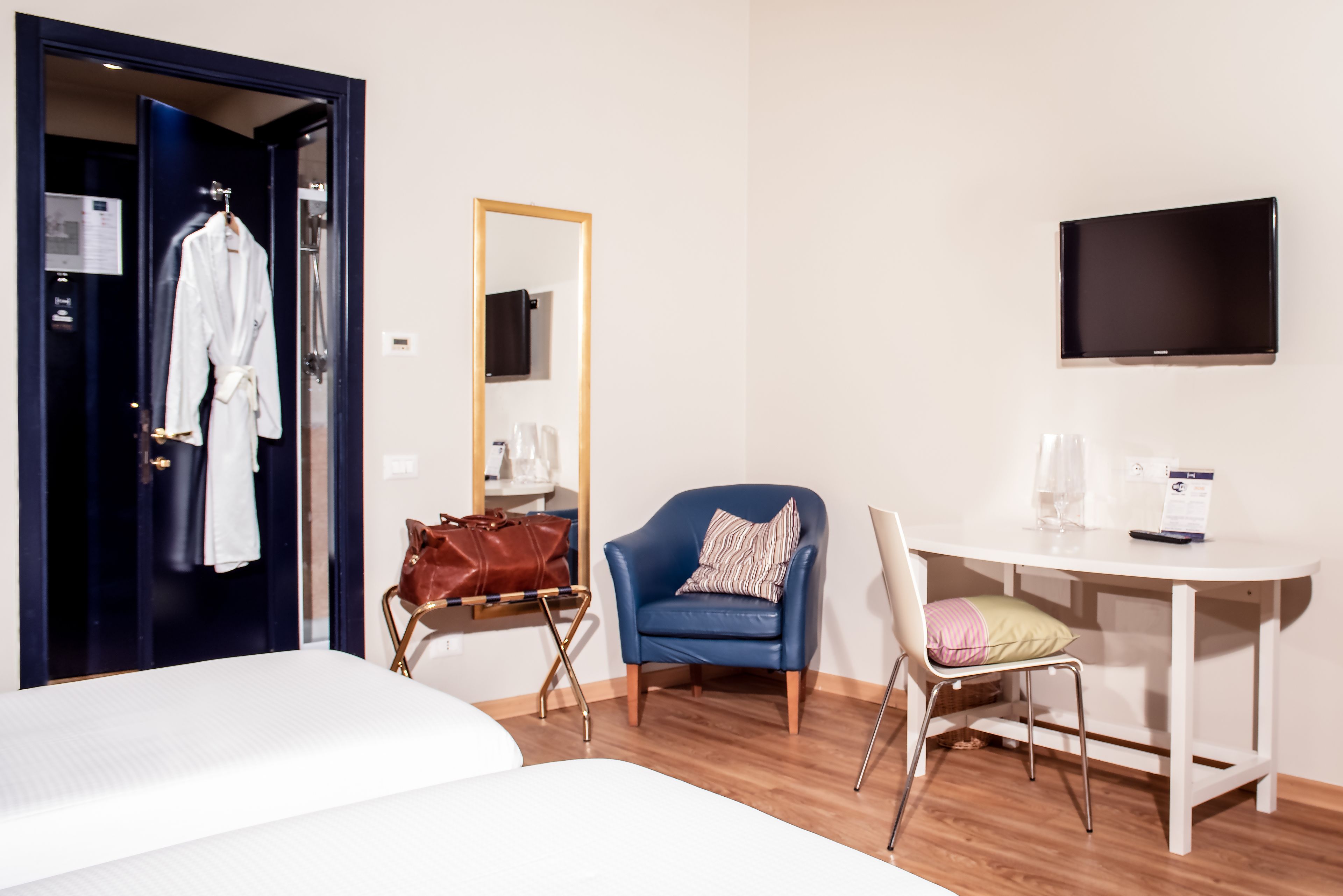 A hotel room with a bed, a desk with a chair, a TV, a mirror, and a wardrobe.