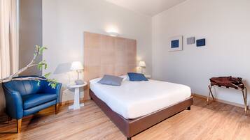 Quarto de hotel moderno com uma cama grande, um sofá azul, uma mesinha de apoio e uma luminária.