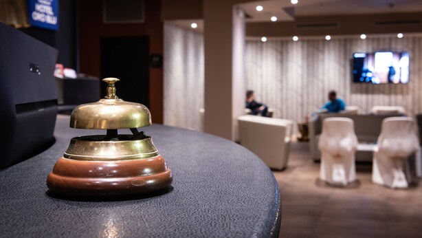 A hotel reception area with a wooden desk, a brass bell, and a seating area with white chairs and a sofa. - Hotel Oro Blu (Milan)