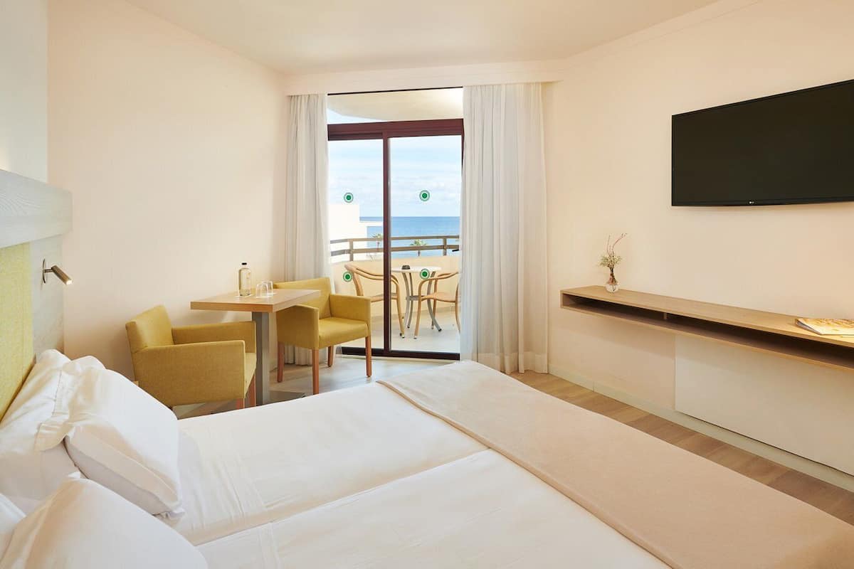 A hotel room with a bed, a desk, two chairs, a TV, and a balcony with a view.