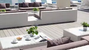 Un área lounge en la azotea con tumbonas, un pilar blanco y vistas al océano.