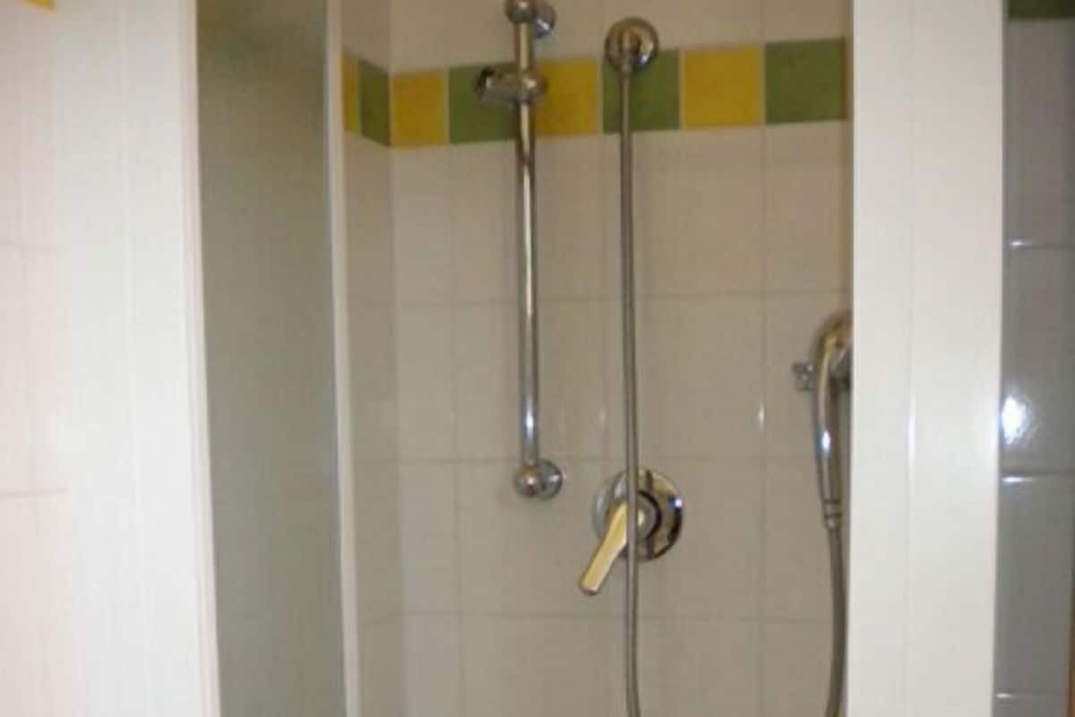 Une douche équipée d’un pommeau de douche à main et d’un robinet fixé au mur.
