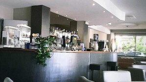 A modern cafe interior with a curved counter, seating area, and a ceiling vent. - Hotel Prater (Cesenatico)