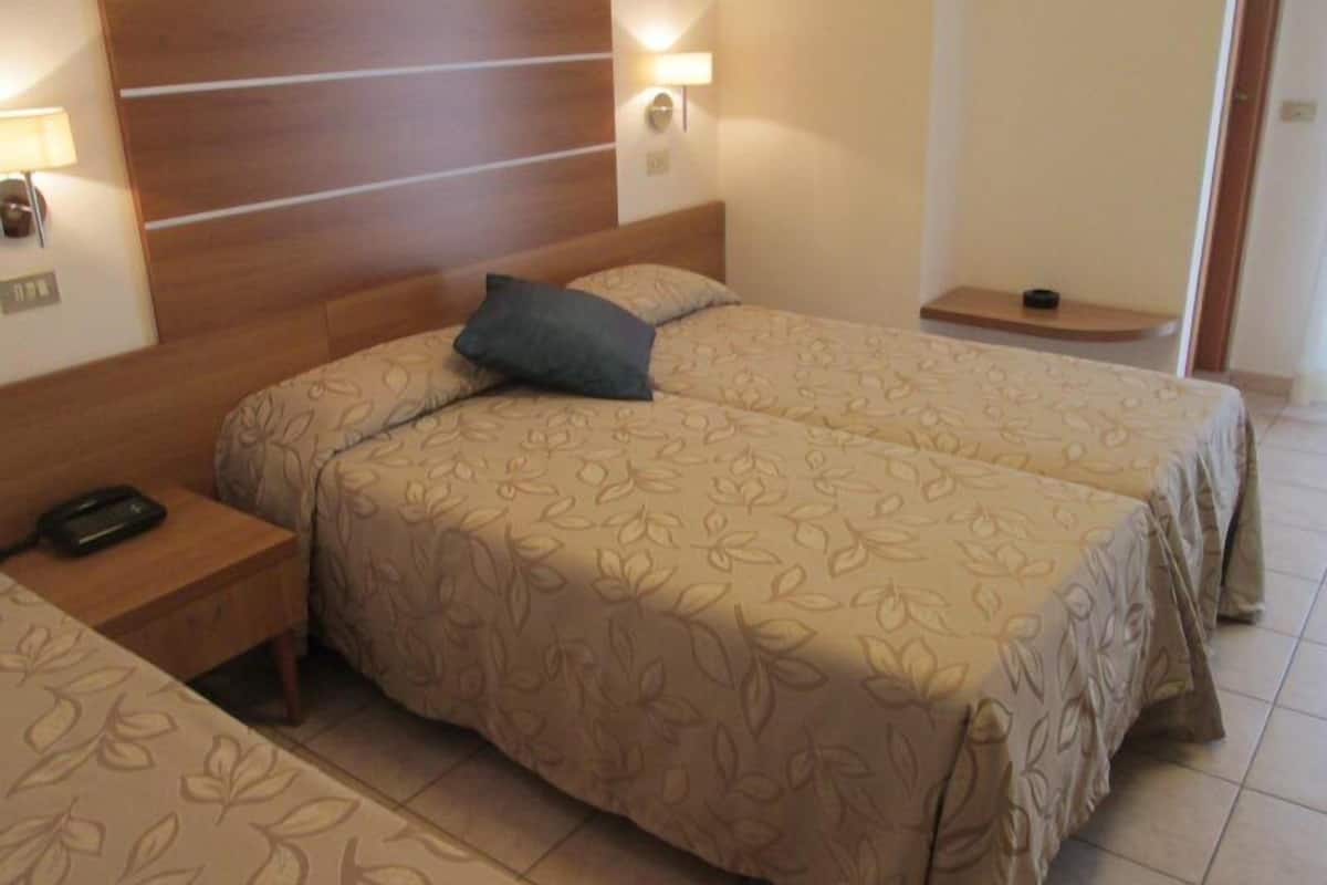 Une chambre d’hôtel avec deux lits, une tête de lit en bois, des lampes de chevet, un téléphone sur la table de chevet et une petite table avec une lampe.