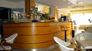 A reception area with a curved counter, a coffee machine, and a seating area with chairs and tables. - Hotel Prater (Cesenatico)