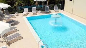 Une piscine rectangulaire à l’eau d’un bleu cristallin, entourée de chaises longues blanches et de parasols.
