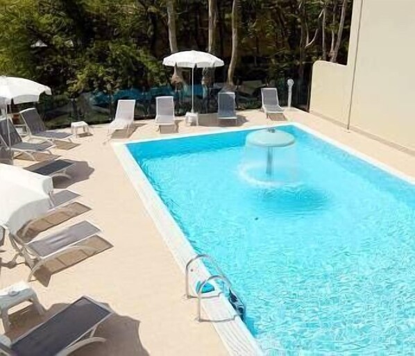 A rectangular swimming pool with clear blue water, surrounded by white lounge chairs and umbrellas. - Hotel Prater (Cesenatico)
