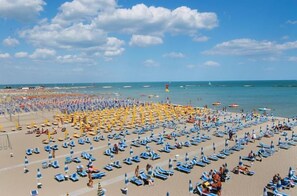 A beach with rows of sun loungers and umbrellas, boats in the water, and a clear sky. - Hotel Prater (Cesenatico)