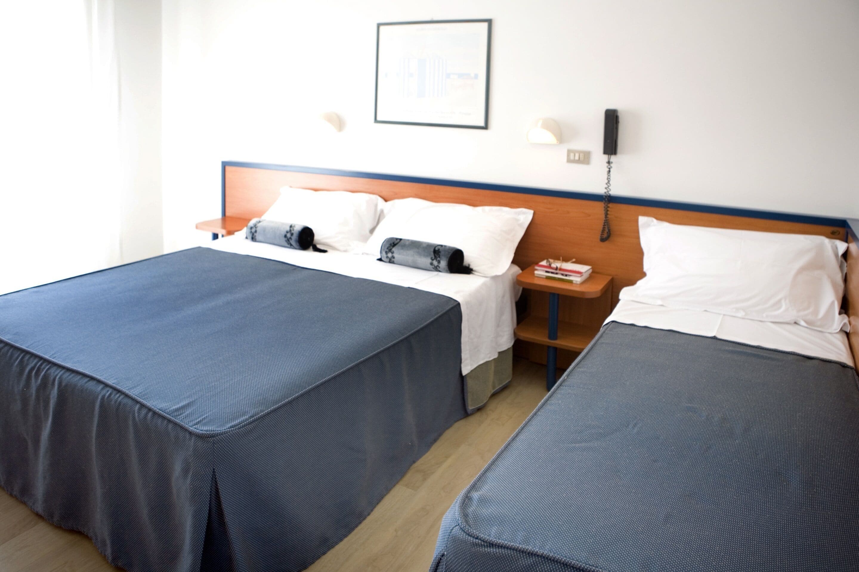 Een hotelkamer met twee bedden, een houten hoofdbord, een nachtkastje met een lamp, een gecertificeerde lijst aan de muur, en een telefoon aan de wand.