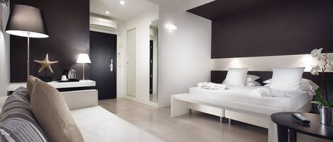A modern hotel room with a large bed, a sofa, a bedside table with a lamp, and a starfish decoration.
