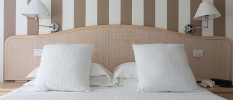 Cama bem arrumada com roupa de cama branca, duas luminárias fixadas na parede e um padrão de listras na parede.