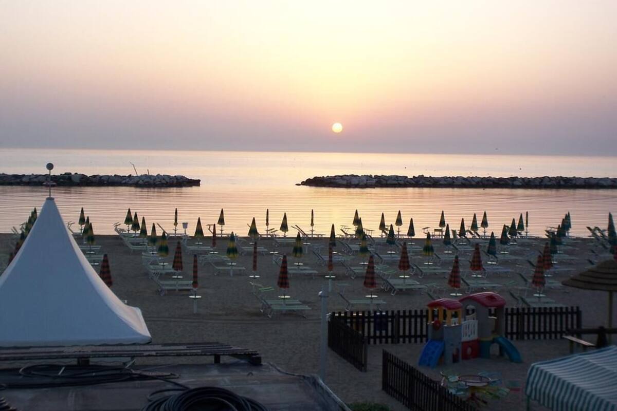 A beach with rows of umbrellas and lounge chairs, a play area, and a tent.