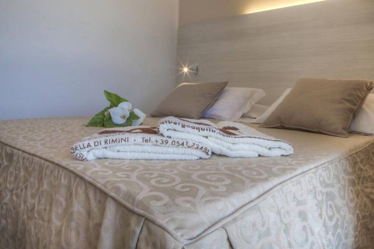 A neatly made bed with a patterned bedspread, two pillows, and a folded towel with a logo and contact information.