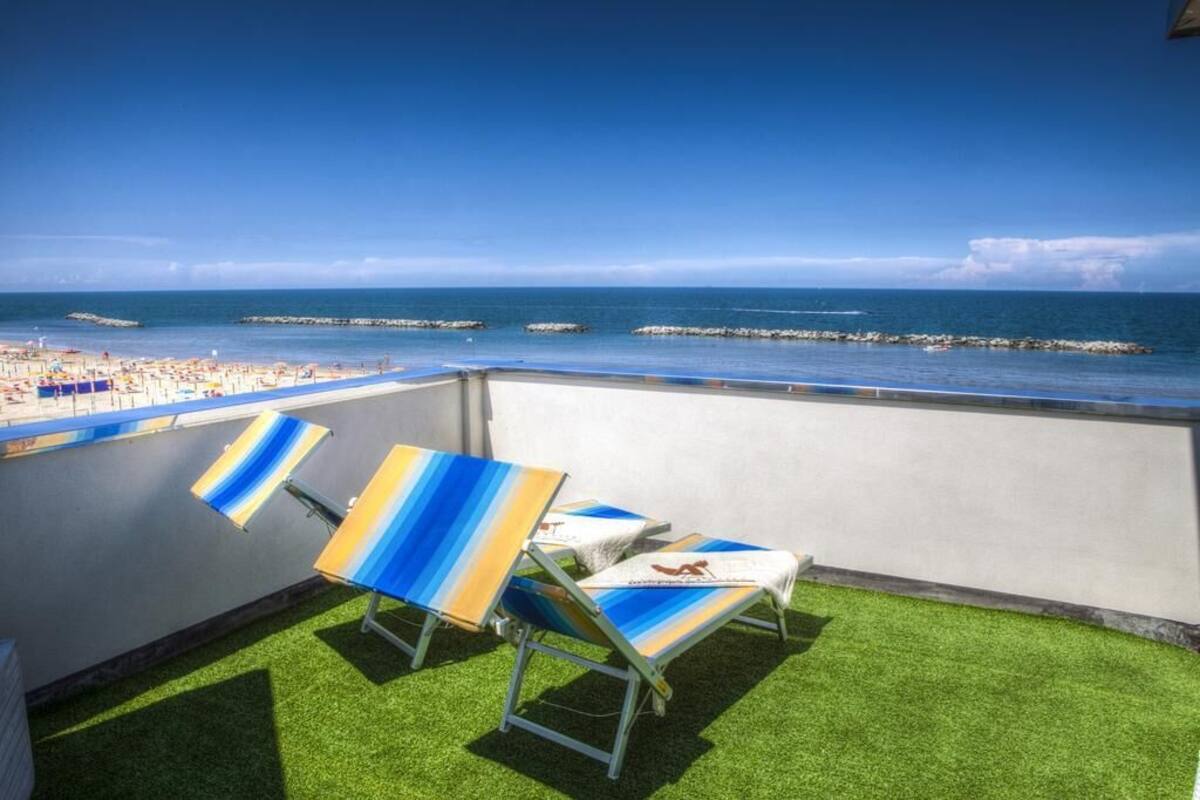 A balcony with artificial grass and two striped lounge chairs.