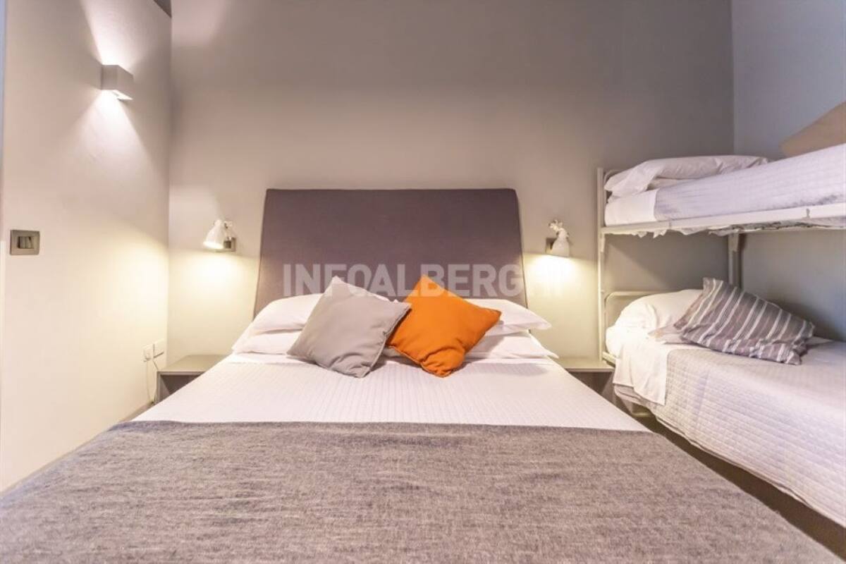 A hotel room with a single bed, two bedside tables, a headboard, and a bunk bed.