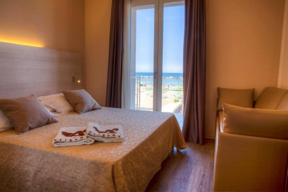 A hotel room with a bed, a chair, and a view of the beach.