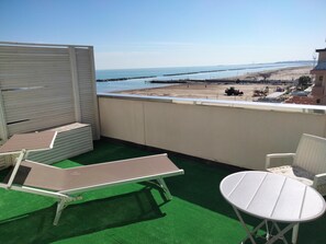 A balcony with green artificial turf, two lounge chairs, and a small table. A view of the beach and sea is visible through the railing. - Albergo Aquila (Rimini)