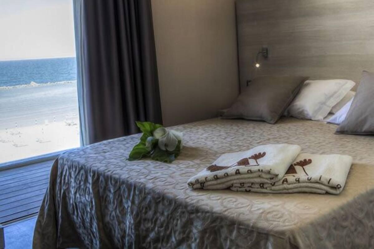 A hotel room with a bed, a view of the beach, and a window with curtains.